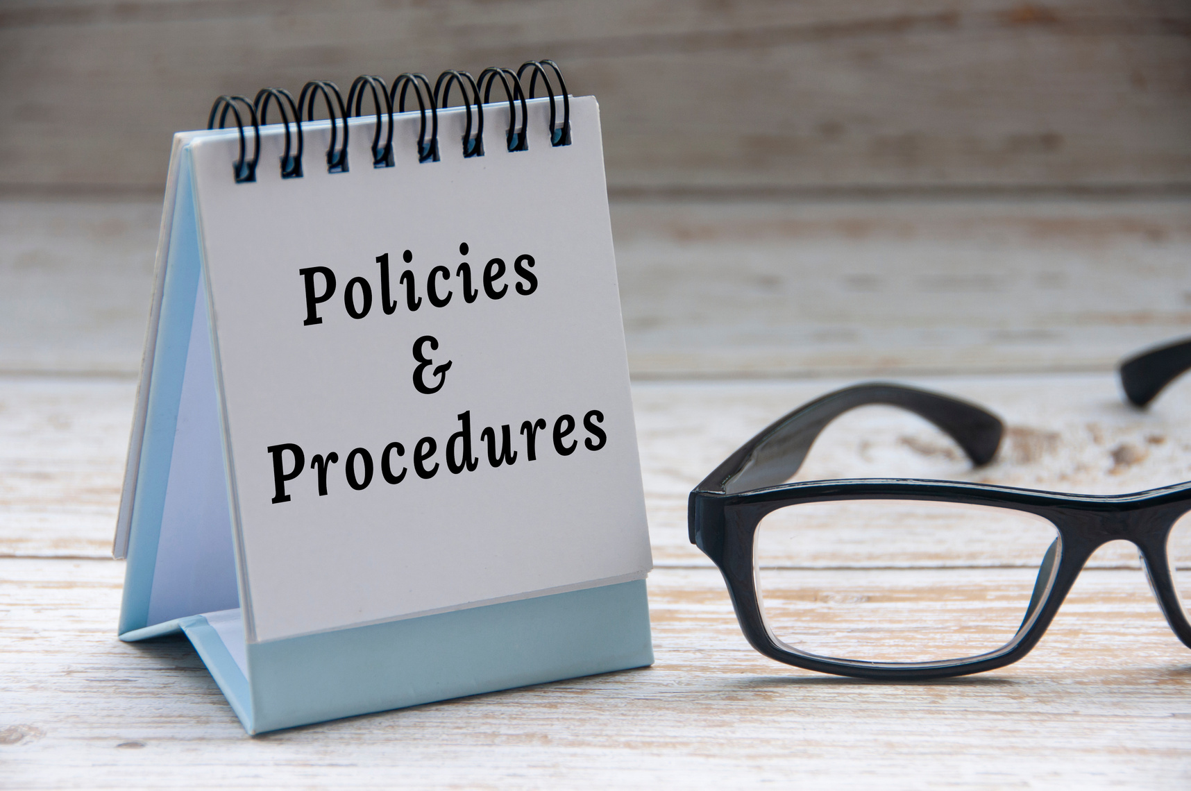Policies and procedures text on notepad with glasses on white wooden cover background.